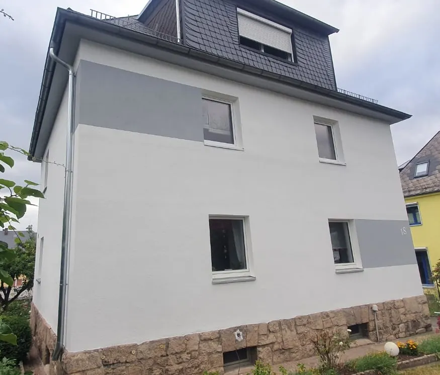 Mehrfamilienhaus mit weiß gestrichener Fassade, grauen Farbflächen und Natursteinsockel