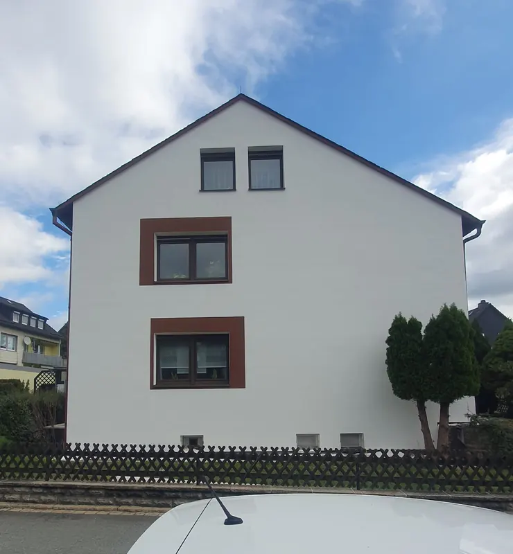 Giebelseite eines Hauses mit weißer Fassade und braunroten Fenstereinfassungen