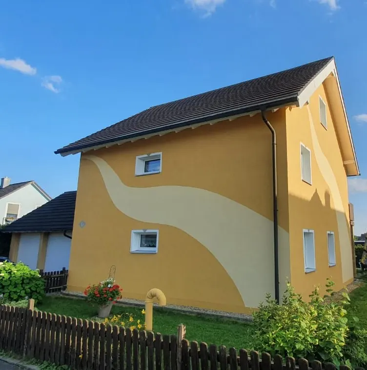 Gelbes Wohnhaus mit geschwungenen hellen Farbflächen in der Fassade