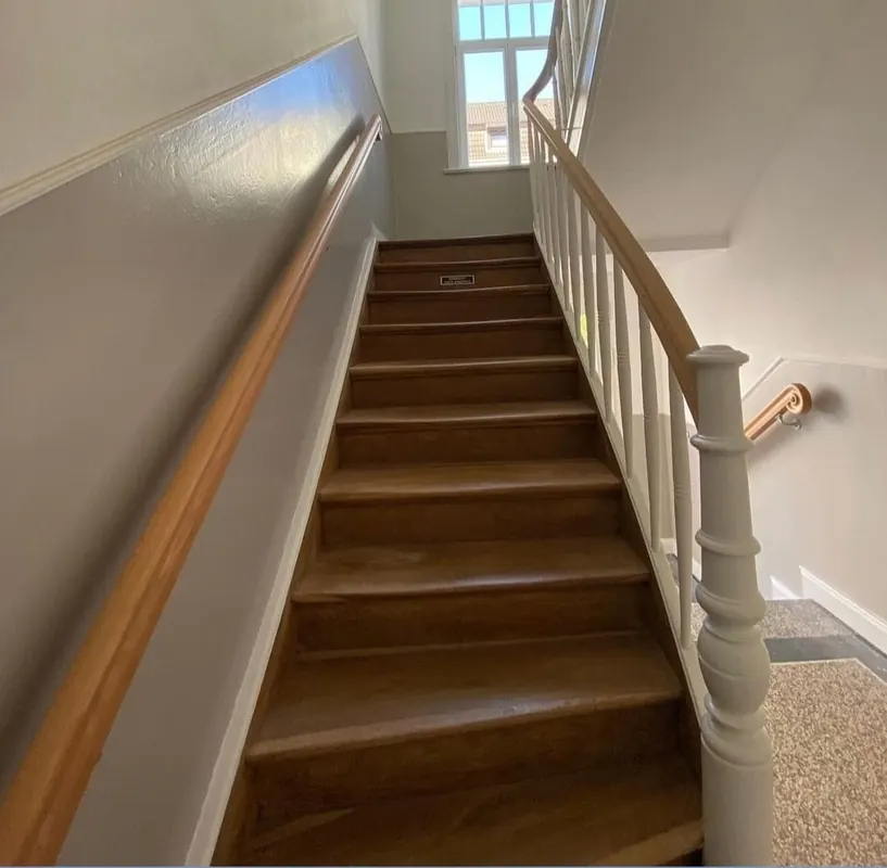 Treppenhaus mit Holztreppe, hellen Wänden und Handlauf