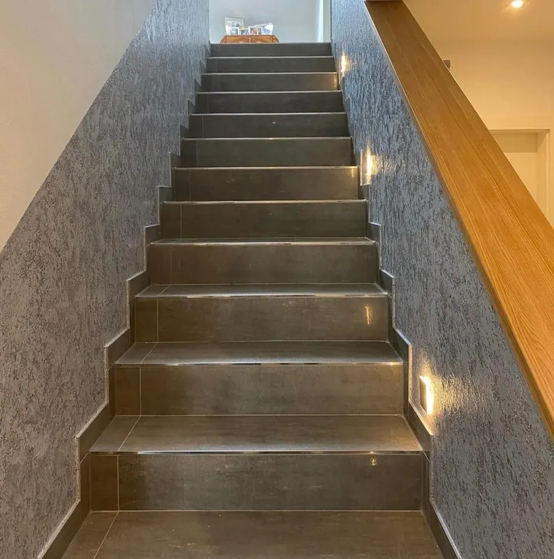 Treppe mit dunklen Stufen neben einer grau strukturierten Wand