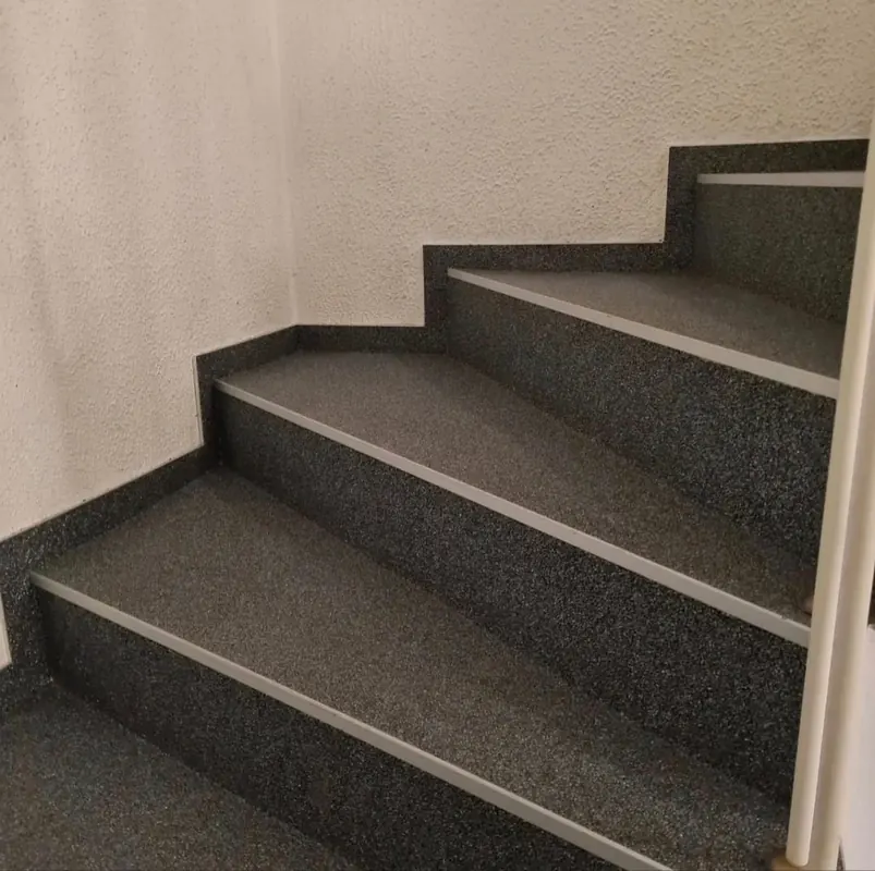 Treppenstufen mit dunklem, körnigem Belag und umlaufender Sockelleiste